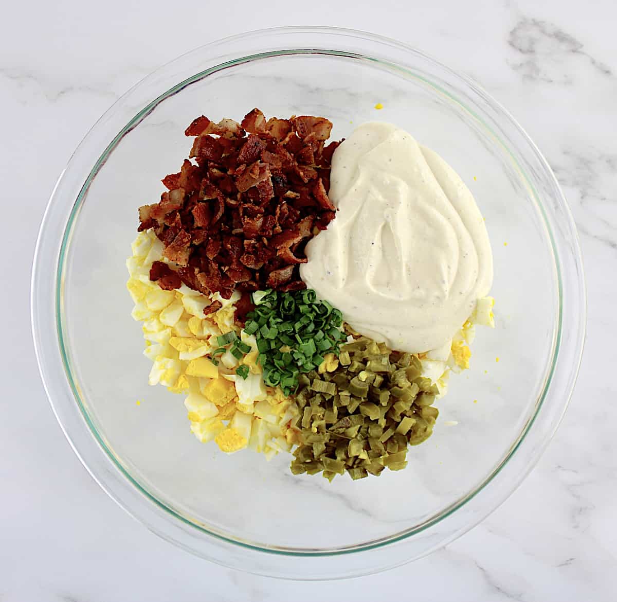 chopped eggs, dressing, crumbed bacon, scallions and jalapenos in glass bowl unmixed