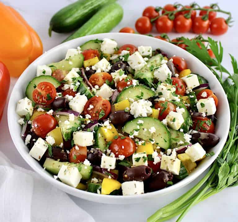 Keto Greek Salad with Dressing in white bowl with veggies in background
