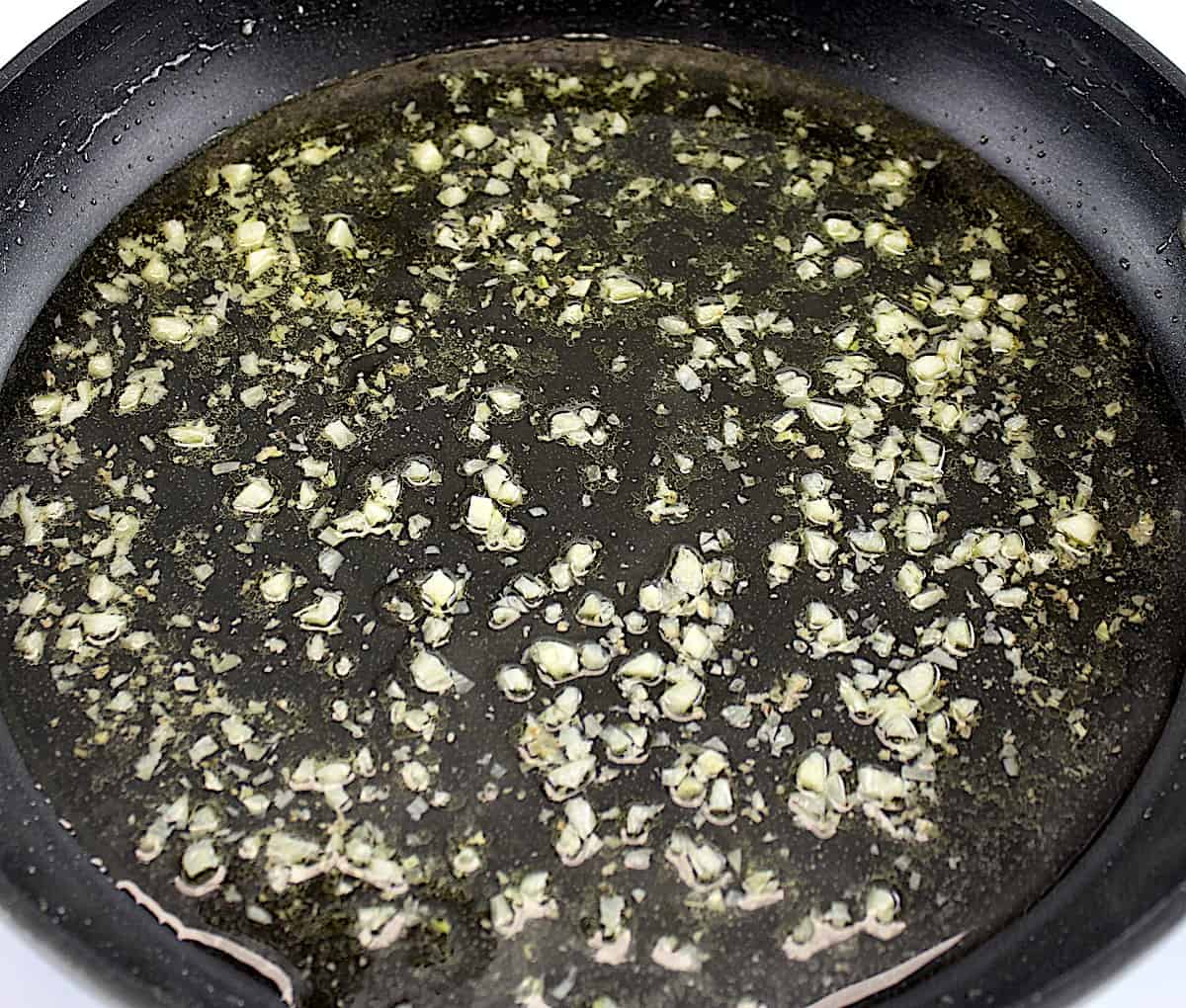 minced garlic with white wine in skillet