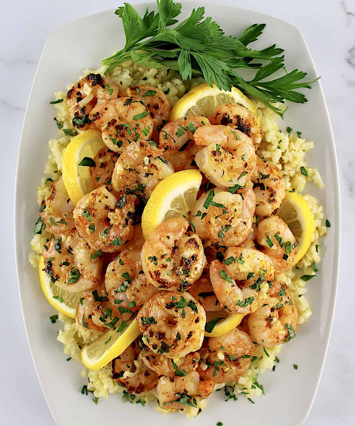 overhead view of Shrimp Scampi with Cauliflower Rice on white plate with parsley garnish and lemon slices