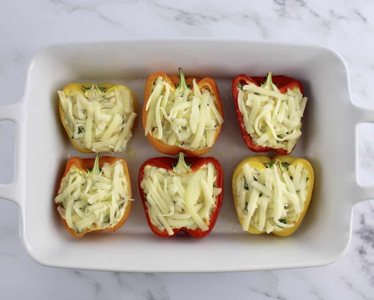 6 Spinach Artichoke Stuffed Peppers in white casserole with shredded mozzarella on top