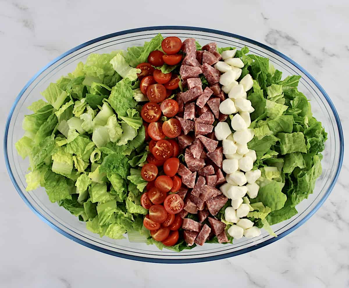 romaine lettuce in oval glass bowl with rows of halved tomatoes mozzarella pearls and chopped soppressata