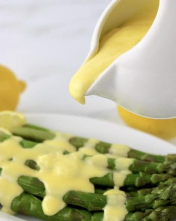 Hollandaise Sauce being poured onto asparagus in white plate