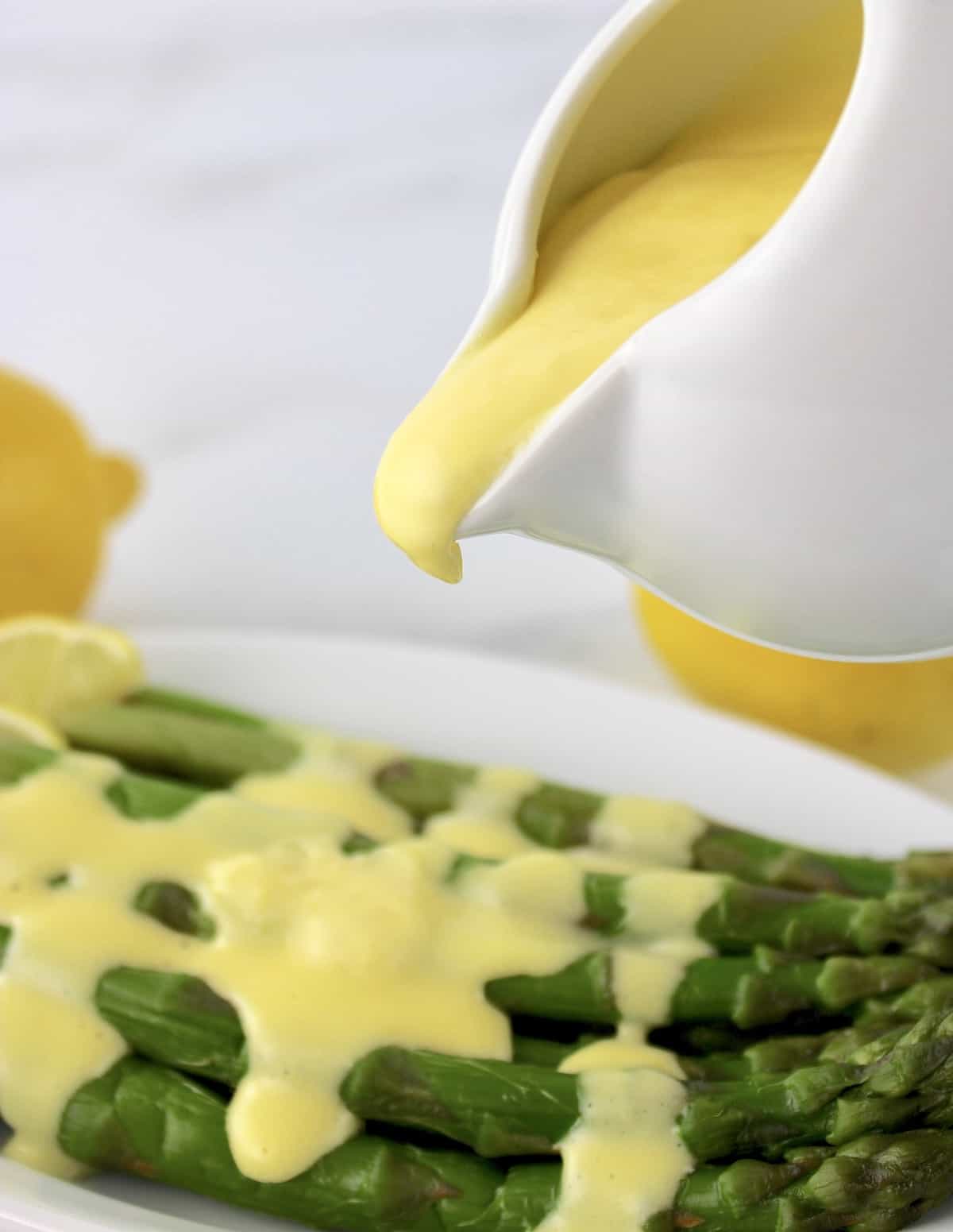 Hollandaise Sauce being poured onto asparagus in white plate