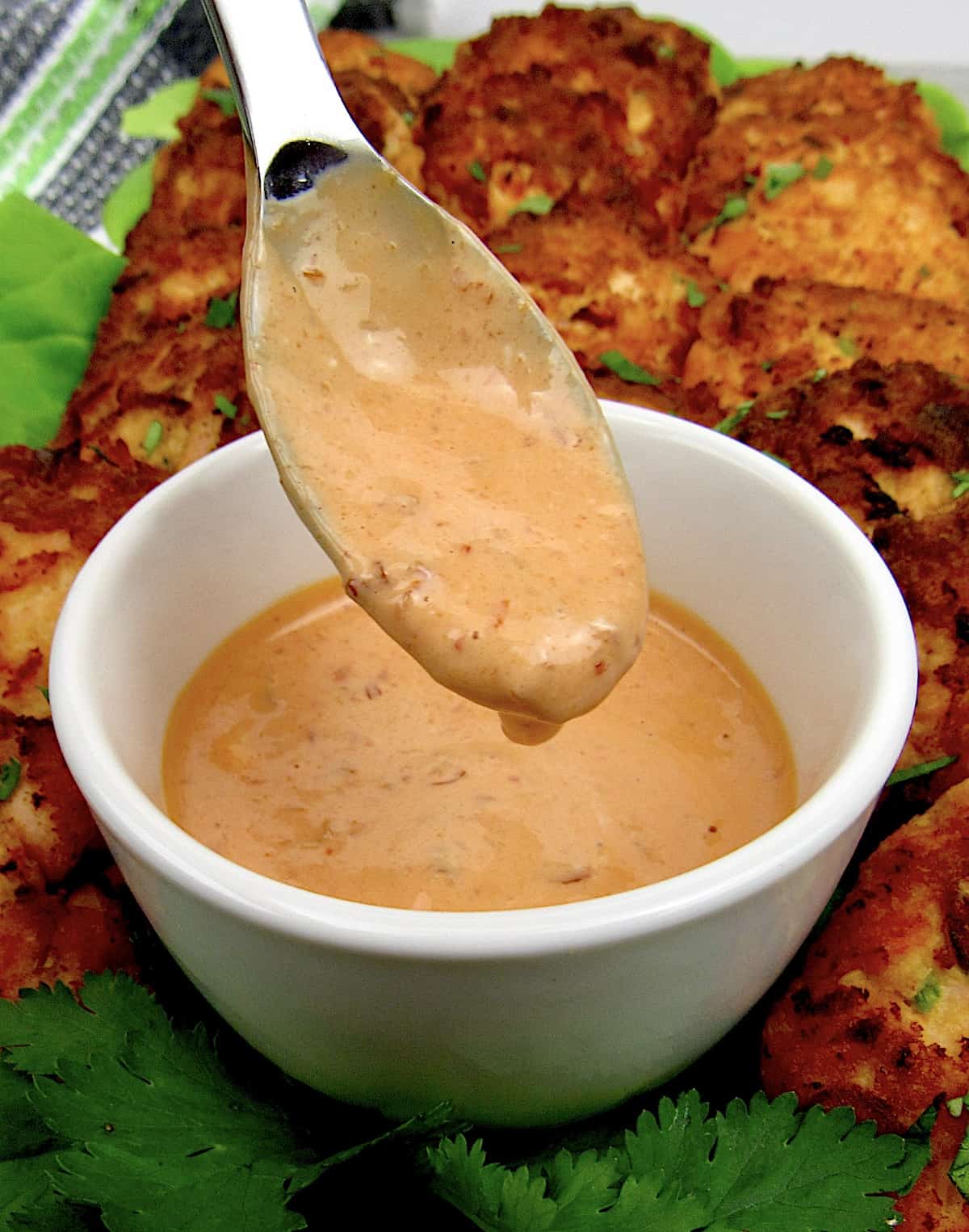 Keto Bang Bang Sauce dripping from spoon with salmon cakes in background