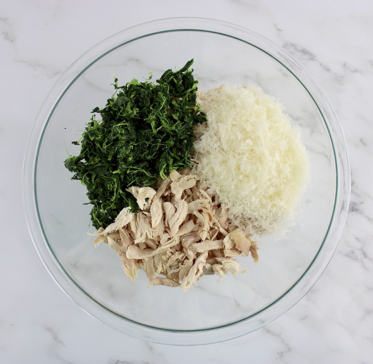 shredded chicken, cooked spinach and grated parmesan cheese in glass bowl unmixed