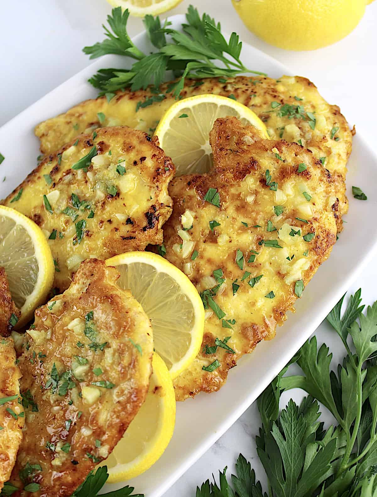 Keto Chicken Francese on white plate with parsley on side and lemon slices