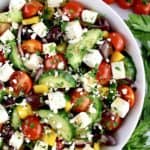 Keto Greek Salad with Dressing in white bowl with parsley and tomatoes in background