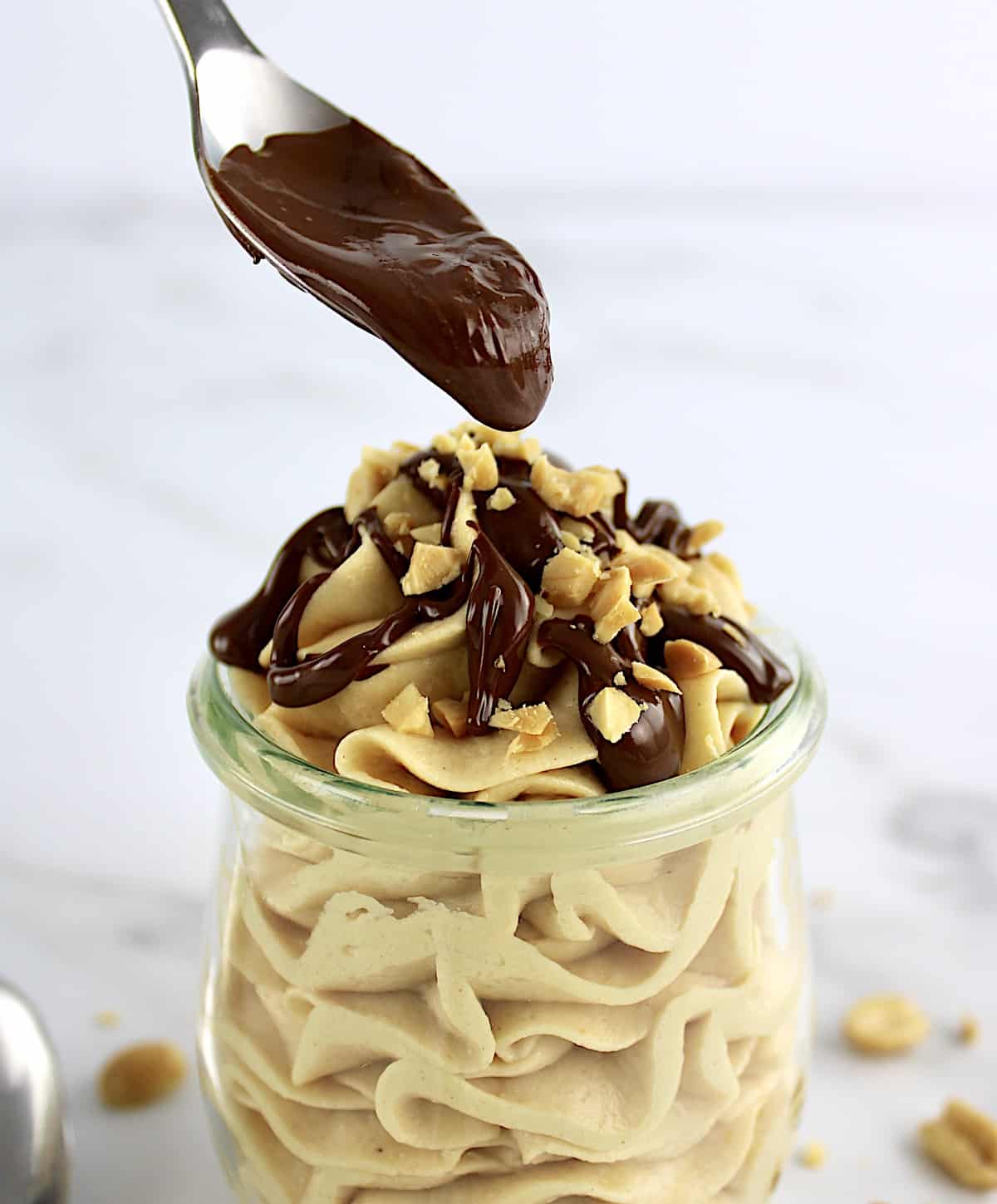 Peanut Butter Mousse in open jar with chocolate sauce being spooned over top
