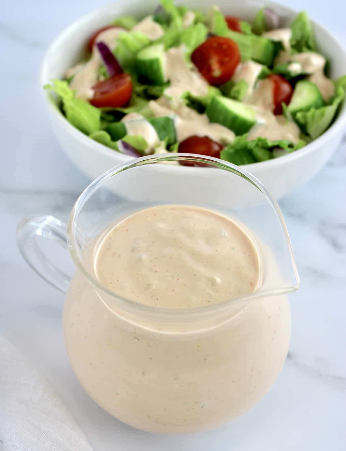 Thousand Island Dressing in glass pitcher with salad in background