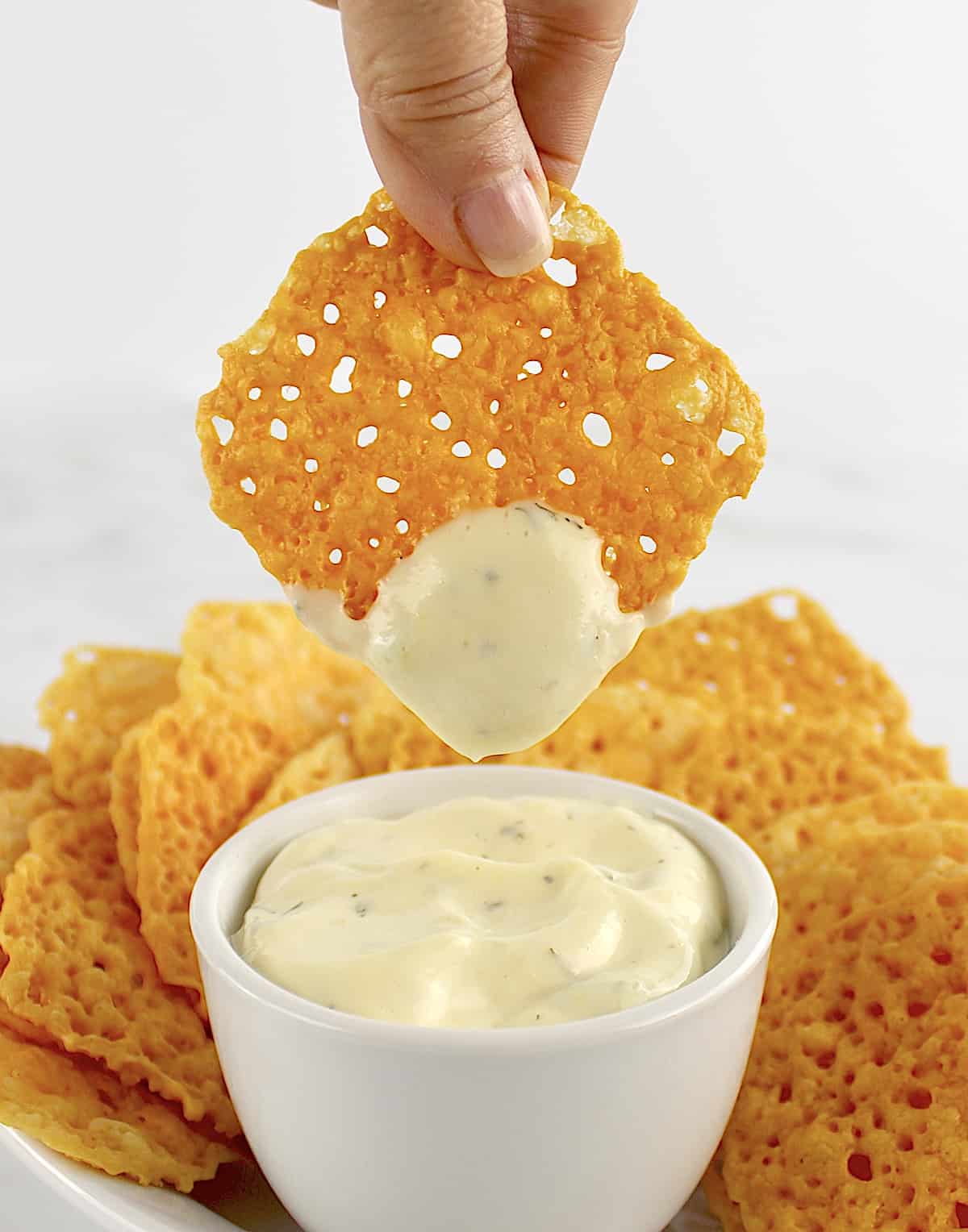 Keto Baked Cheese Crisp Cracker being dipped into dip