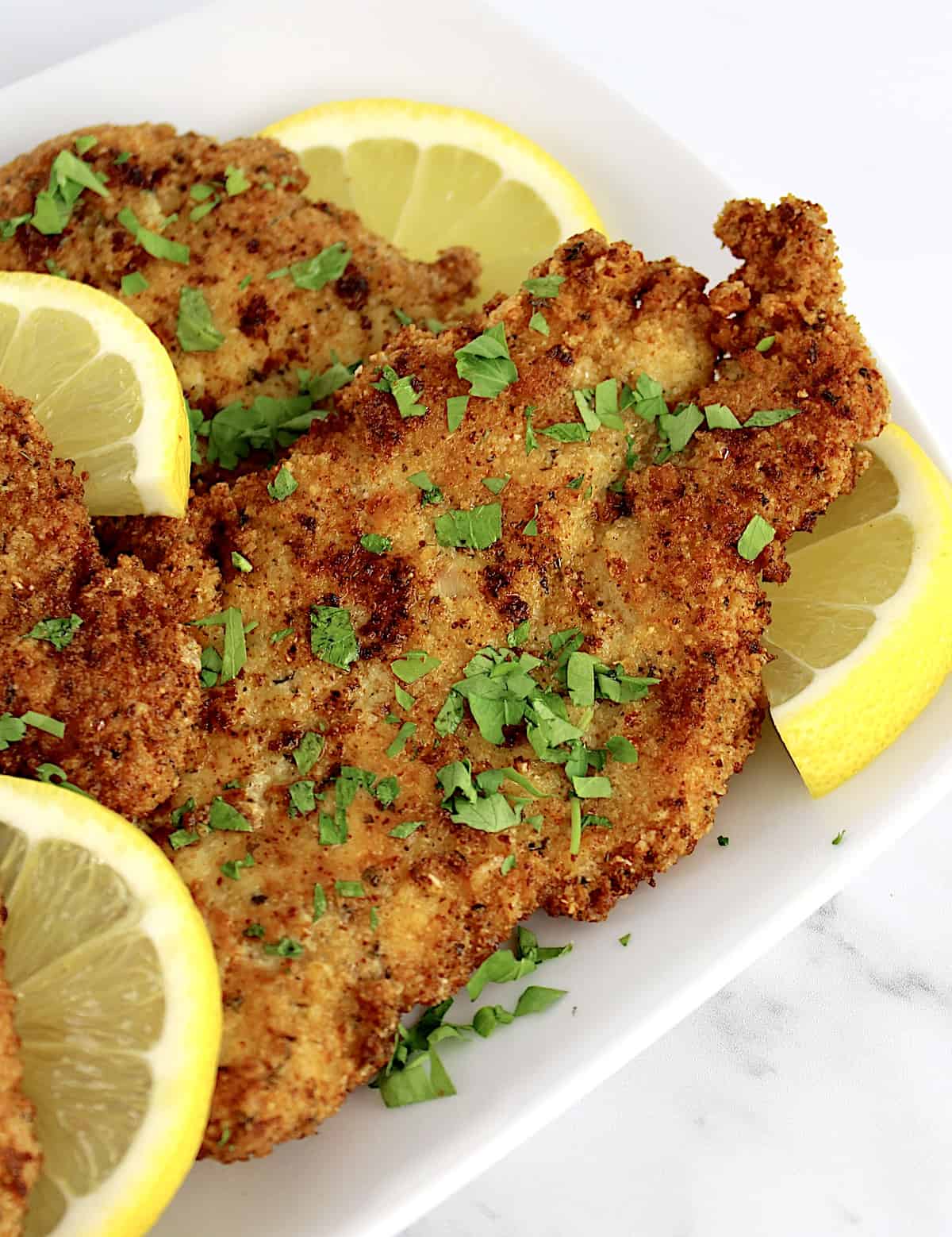 closeup of Keto Chicken Milanese on white plate with lemon slices
