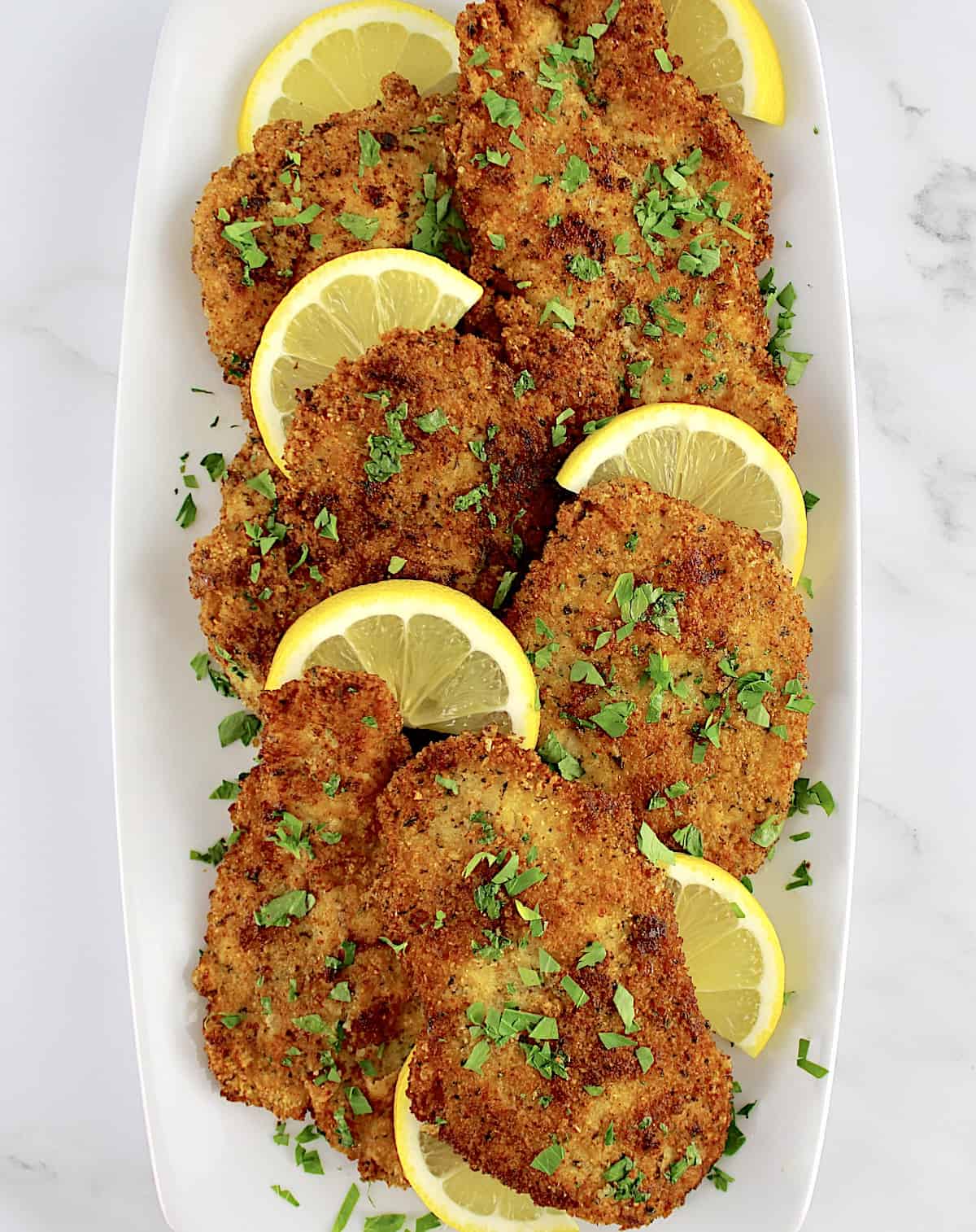 overhead view of closeup of Keto Chicken Milanese on white plate with lemon slices