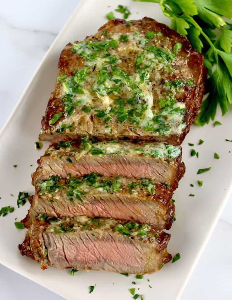 Air Fryer Steak sliced on white plate with parsley butter on top