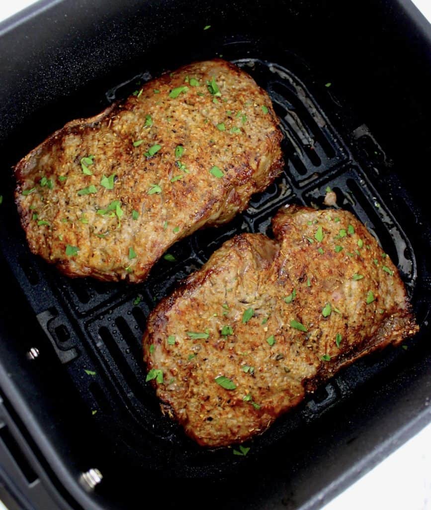 2 Air Fryer Steaks in air fryer basket with parsley on top