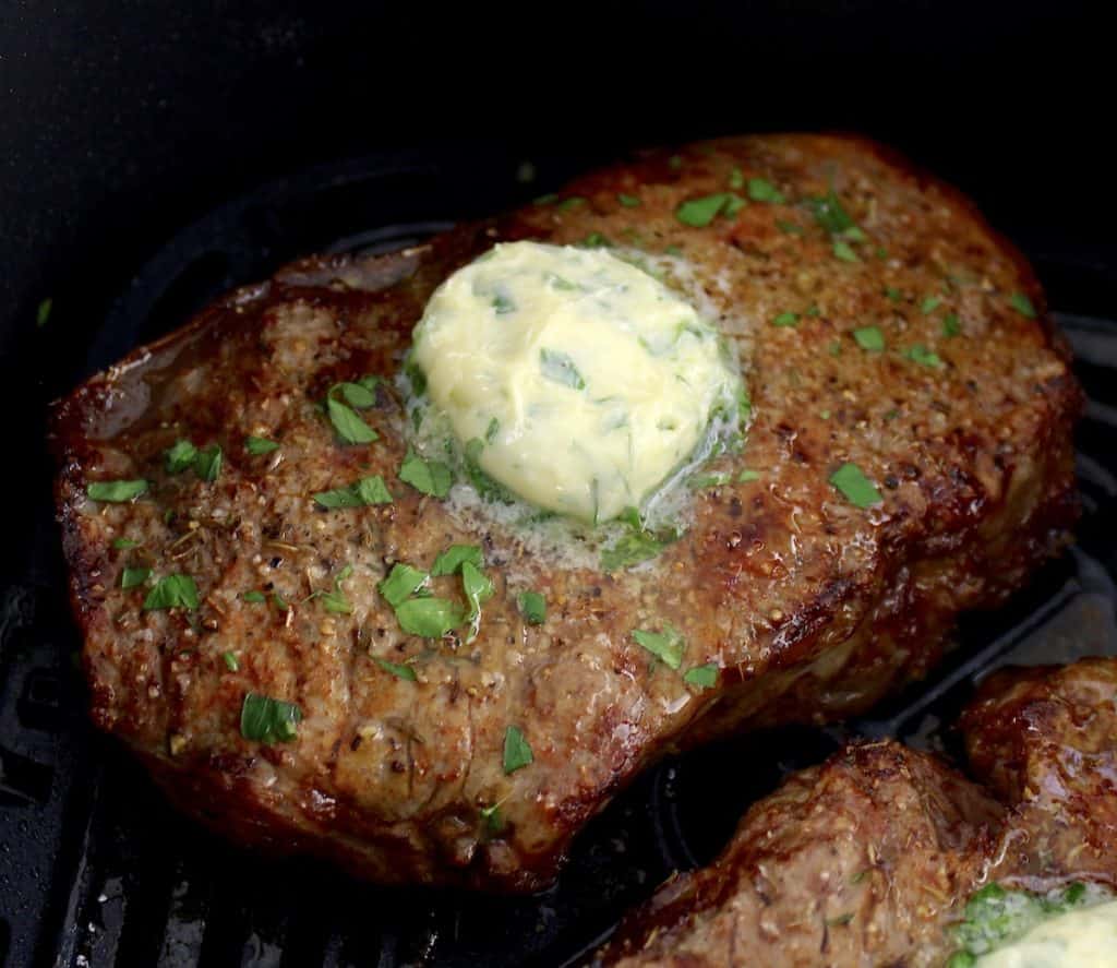 Air Fryer Steak with herb butter and chopped parsley on top inn air fryer basket