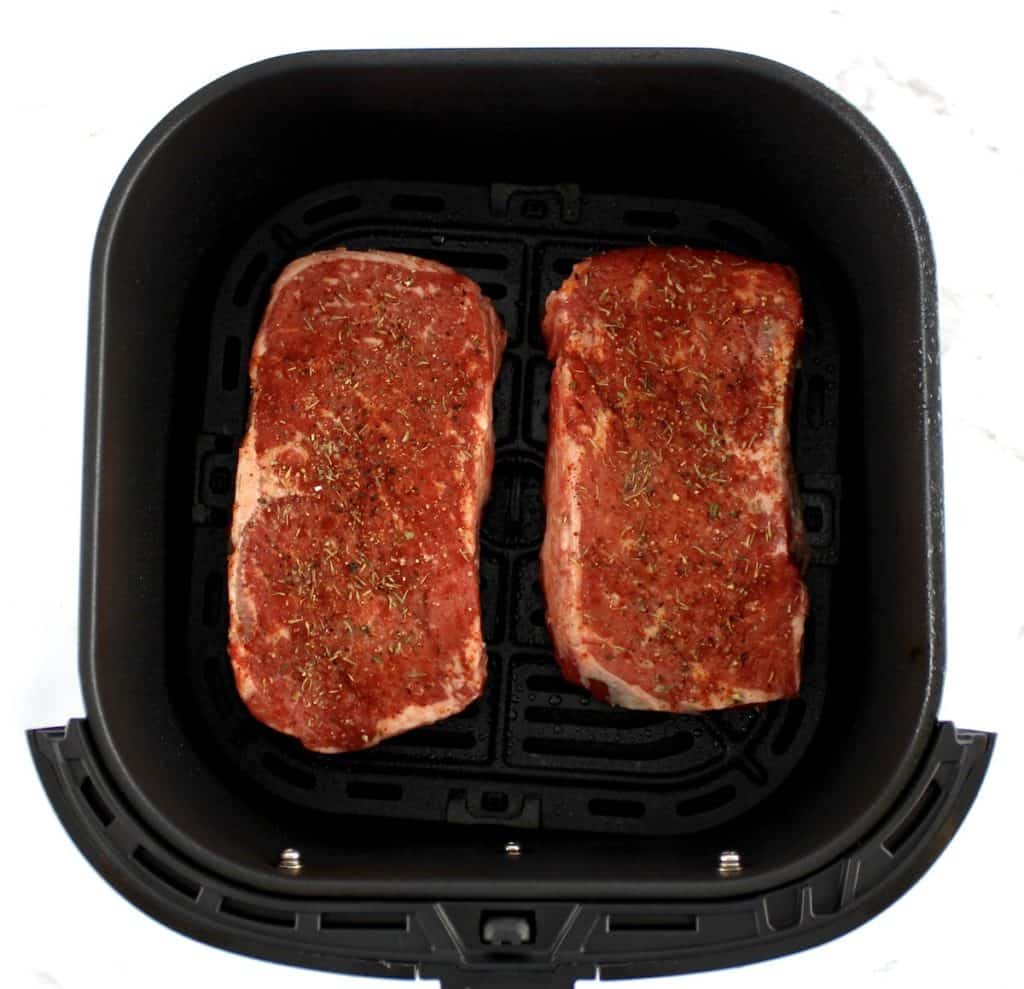 Air Fryer Steak uncooked with spices on top in air fryer basket