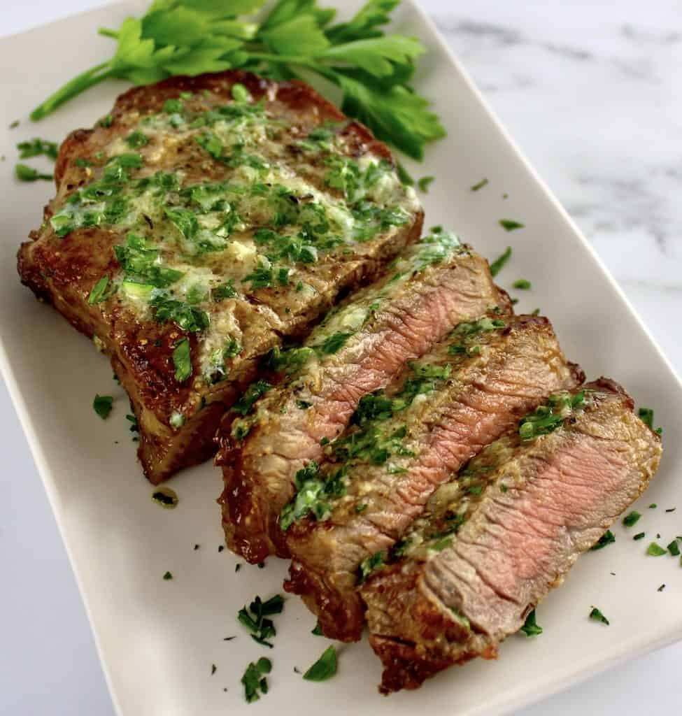Air Fryer Steak sliced on white plate with parsley butter on top