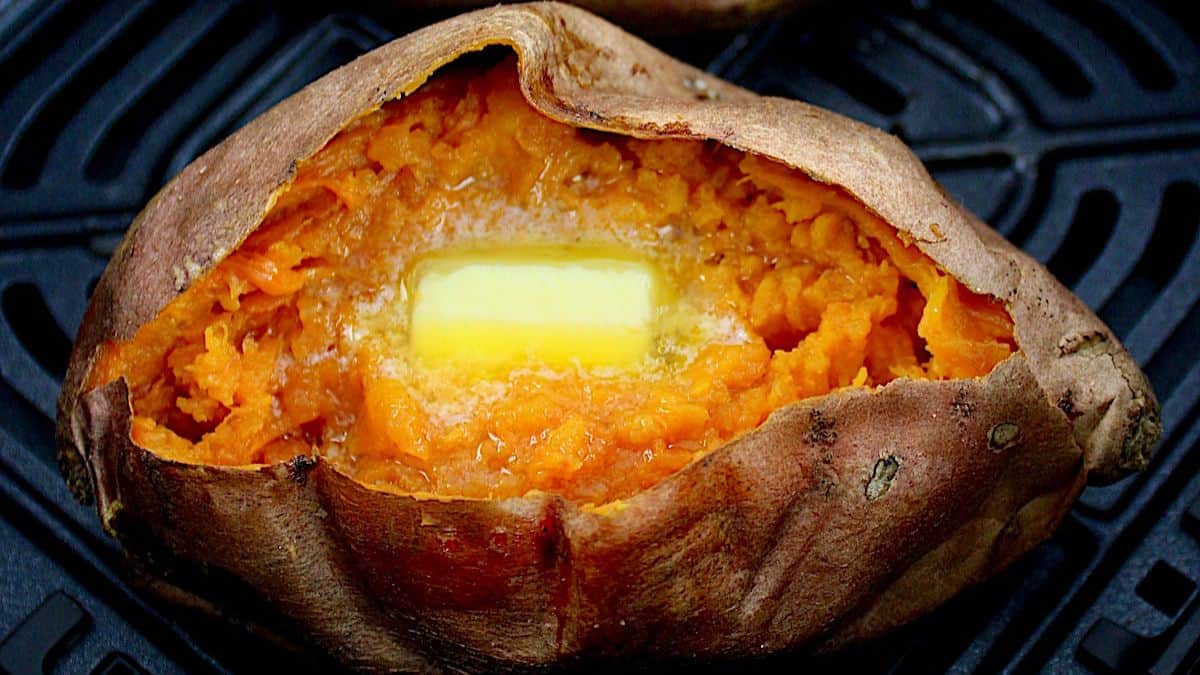 closeup of Air Fryer Sweet Potato in air fryer basket cut open with butter