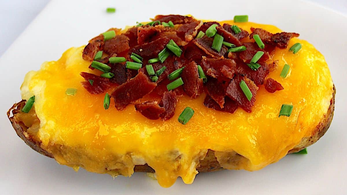 closeup of Air Fryer Twice Baked Potato on white plate with chopped bacon and chives on top