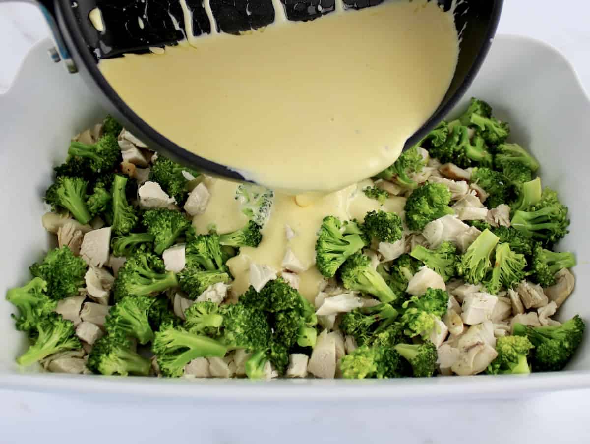 cheese sauce being poured over chopped chicken and broccoli in white casserole