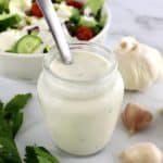 Creamy Garlic Italian Dressing in glass jar with spoon in it and salad in background