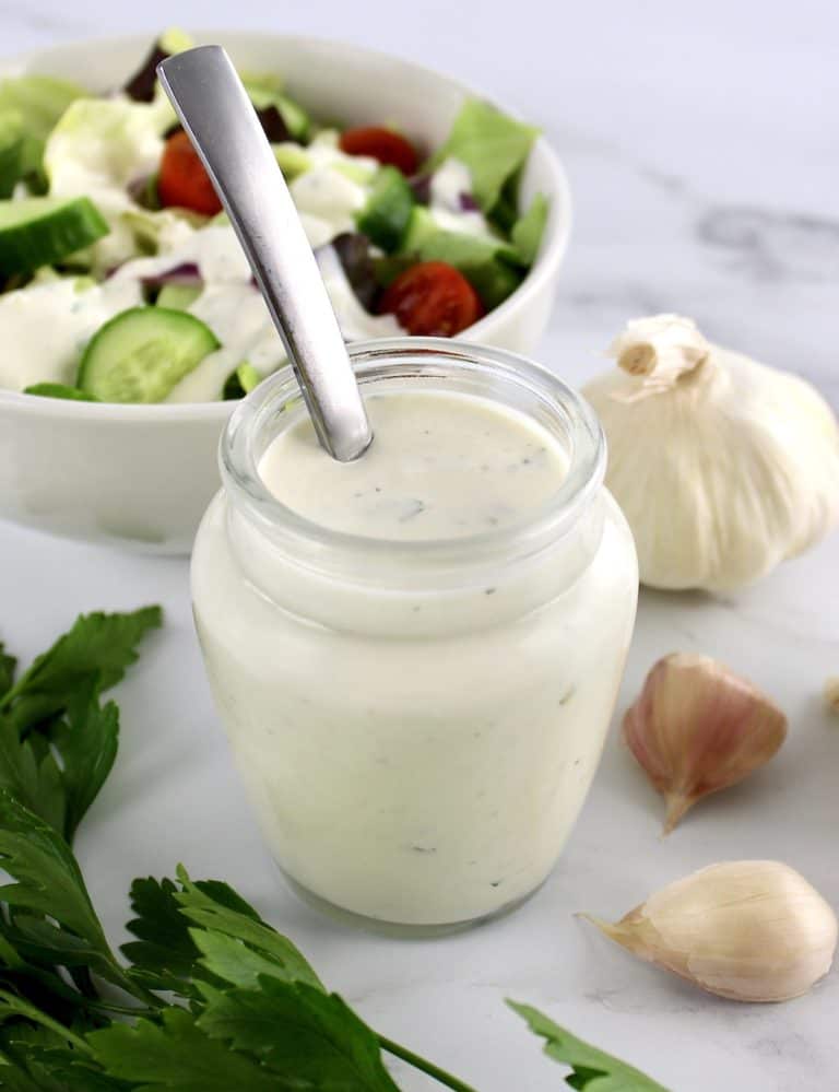 Creamy Garlic Italian Dressing in glass jar with spoon in it and salad in background
