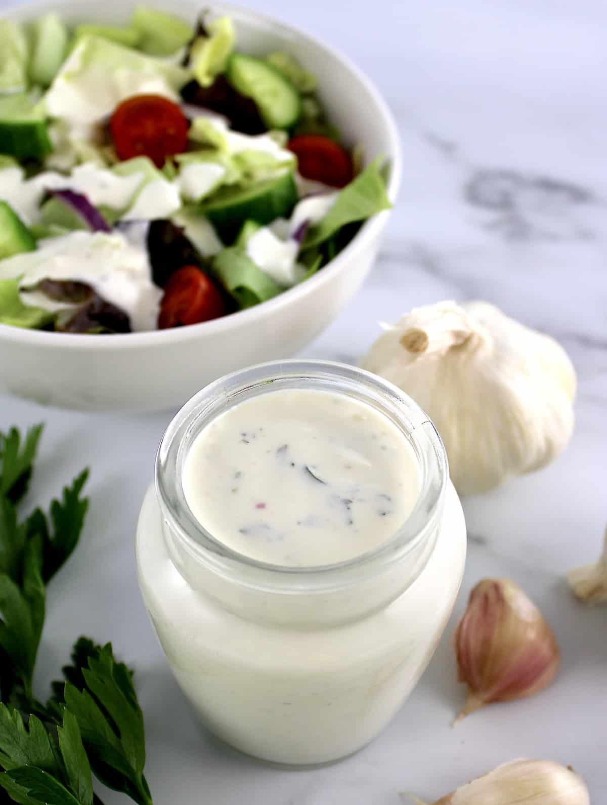 Creamy Garlic Italian Dressing in glass jar with salad in background