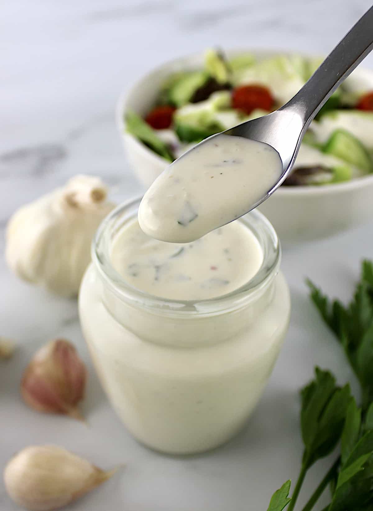 Creamy Garlic Italian Dressing in spoon held up over glass jar
