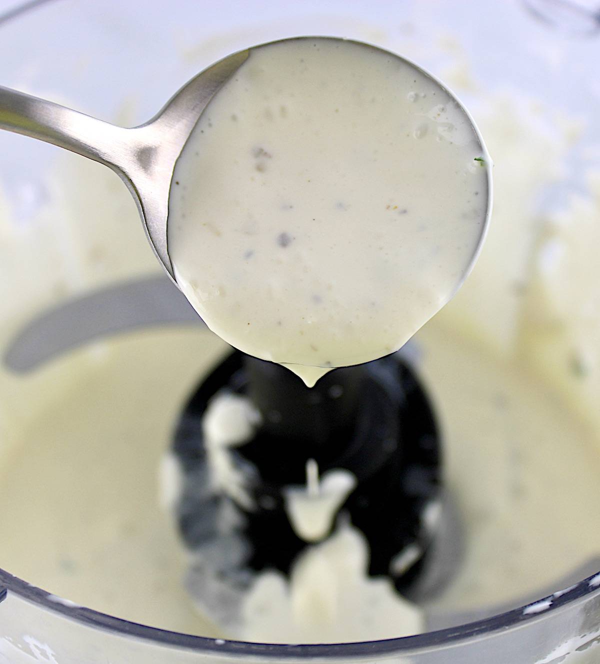 Creamy Garlic Italian Dressing dripping off spoon over food processor bowl