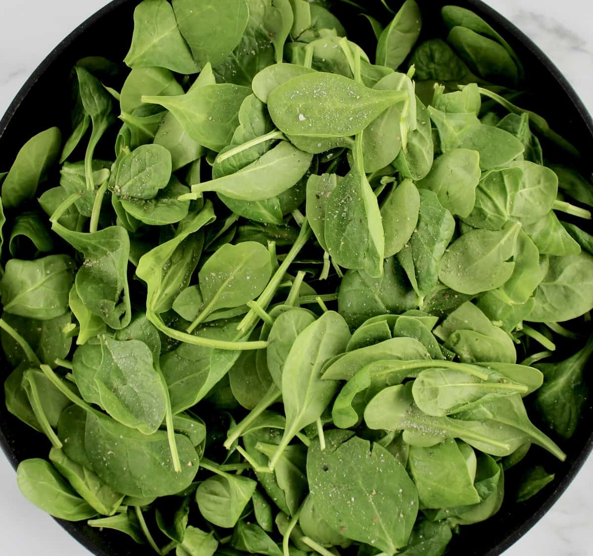 raw baby spinach with salt and pepper on top in skillet