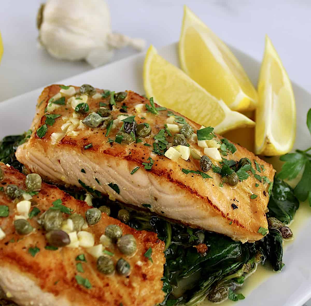 closeup of Salmon Piccata with Spinach and lemon wedges on white plate