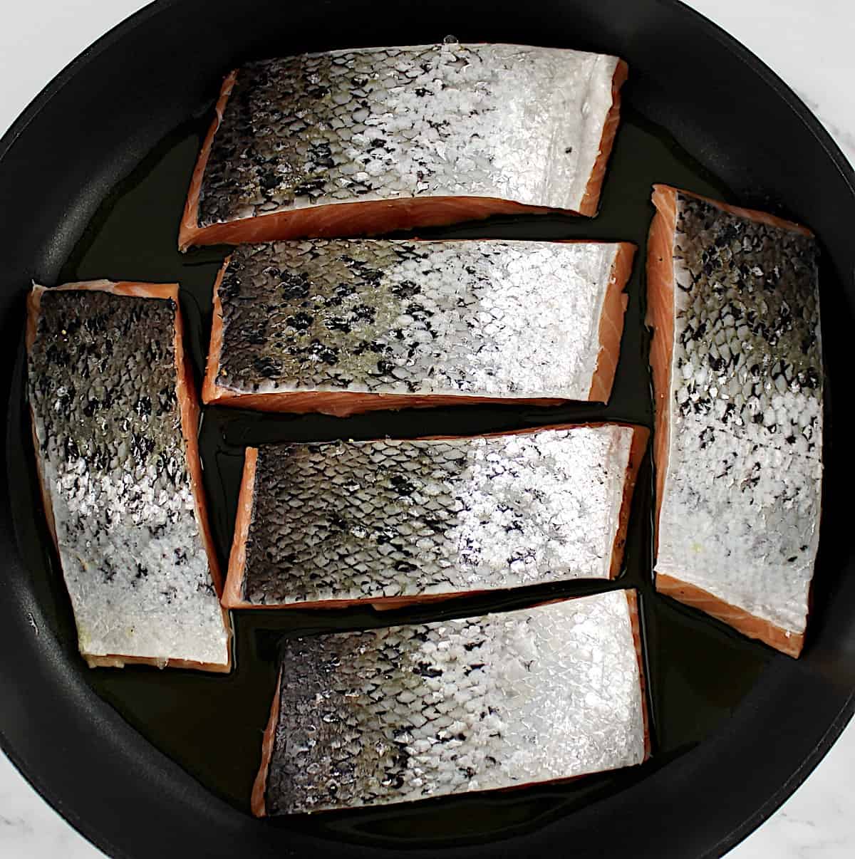 6 pieces of salmon cooking in skillet with skin side up