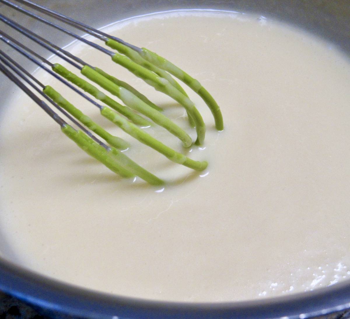 Keto Sweetened Condensed Milk in saucepan with green whisk