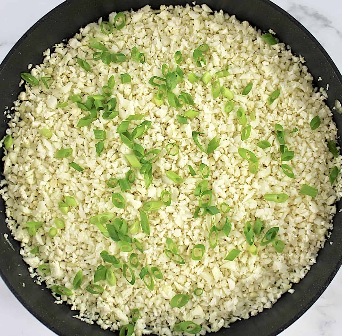 cauliflower rice and chopped scallions in skillet