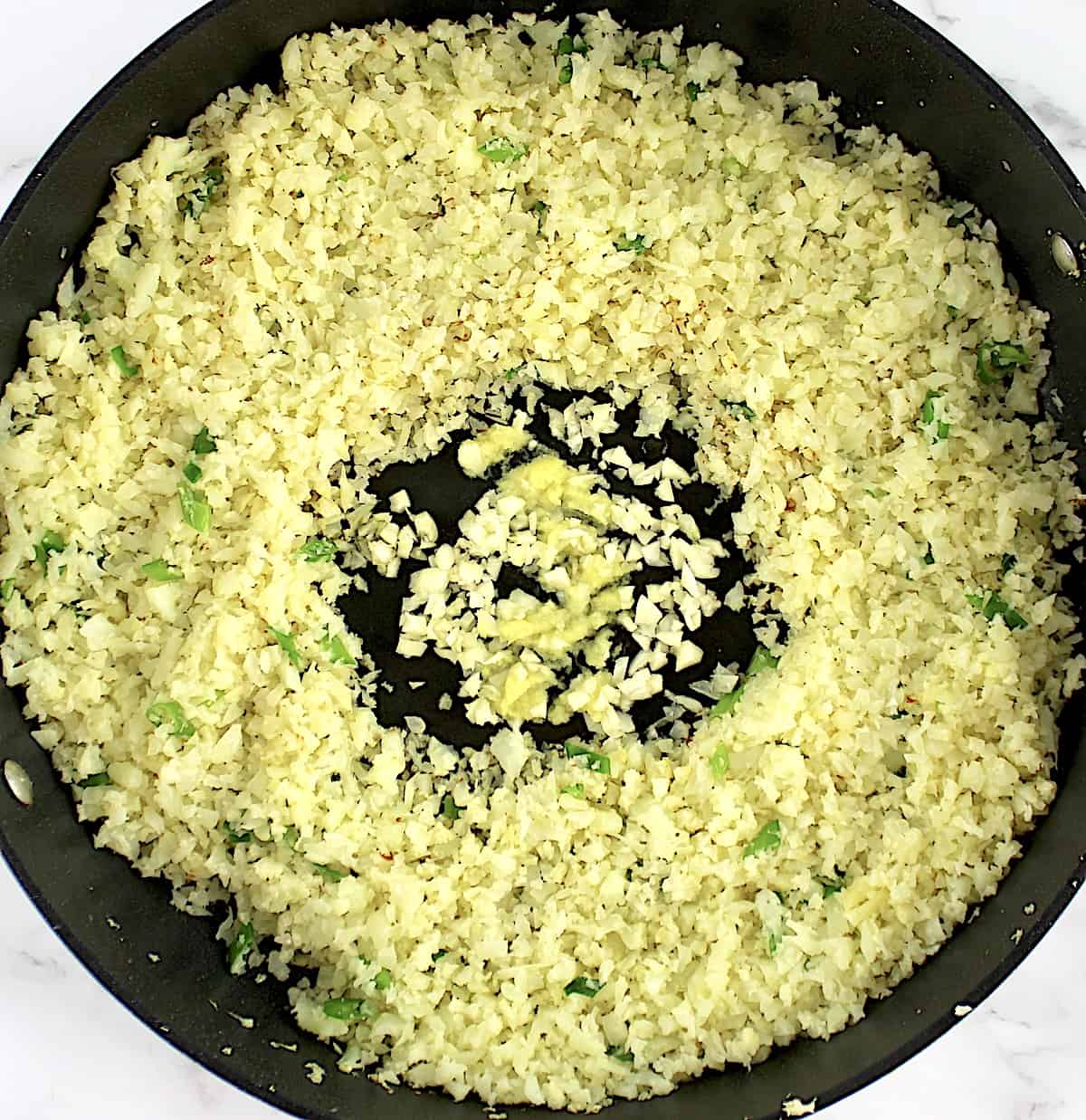 cauliflower rice in skillet with minced garlic and ginger in the center