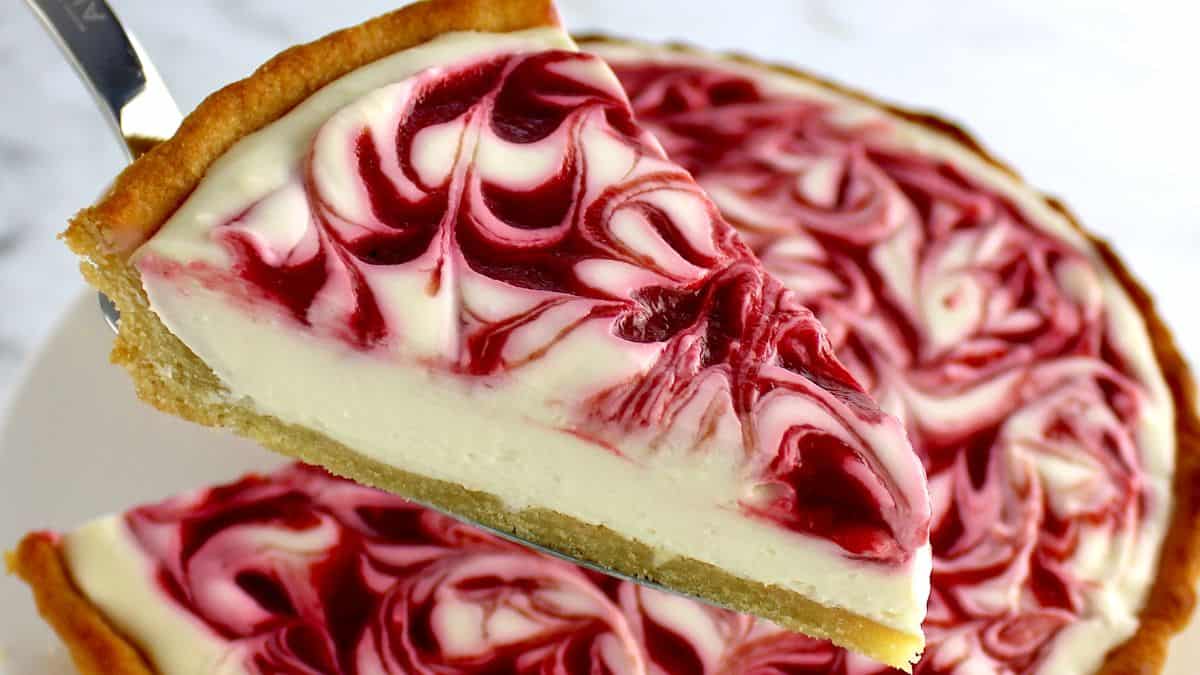 white chocolate raspberry cheesecake slice held up over cheesecake