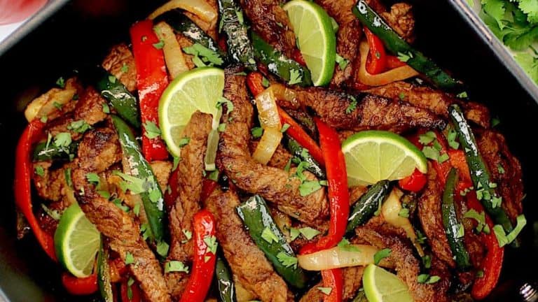 overhead view of Air Fryer Steak Fajitas in air fryer basket with lime slices and chopped cilantro garnish