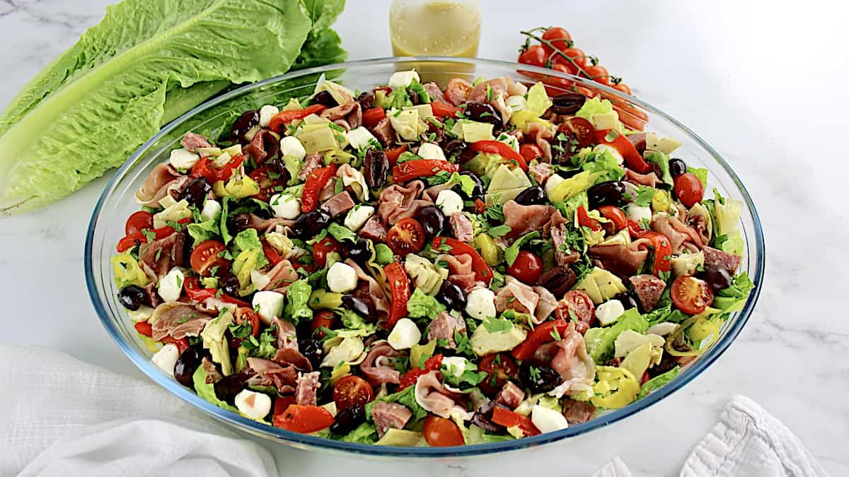 Antipasto Salad with dressing, lettuce and tomatoes in background