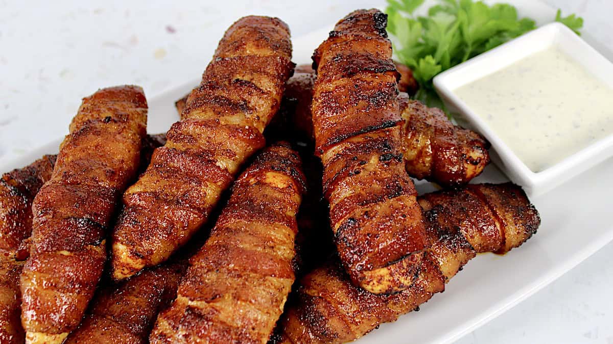 Bacon Wrapped Air Fryer Chicken Tenders on white plate with ranch dressing in small white bowl on site