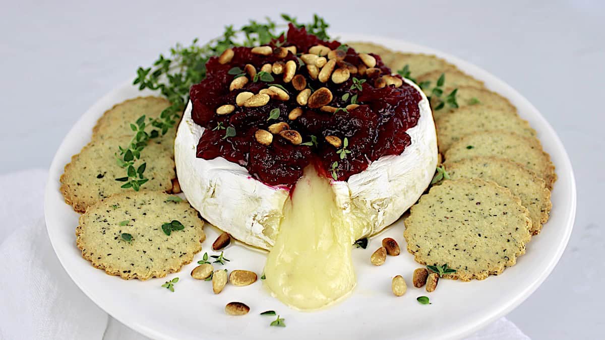 Baked Brie with Cranberry with crackers all around on white plate