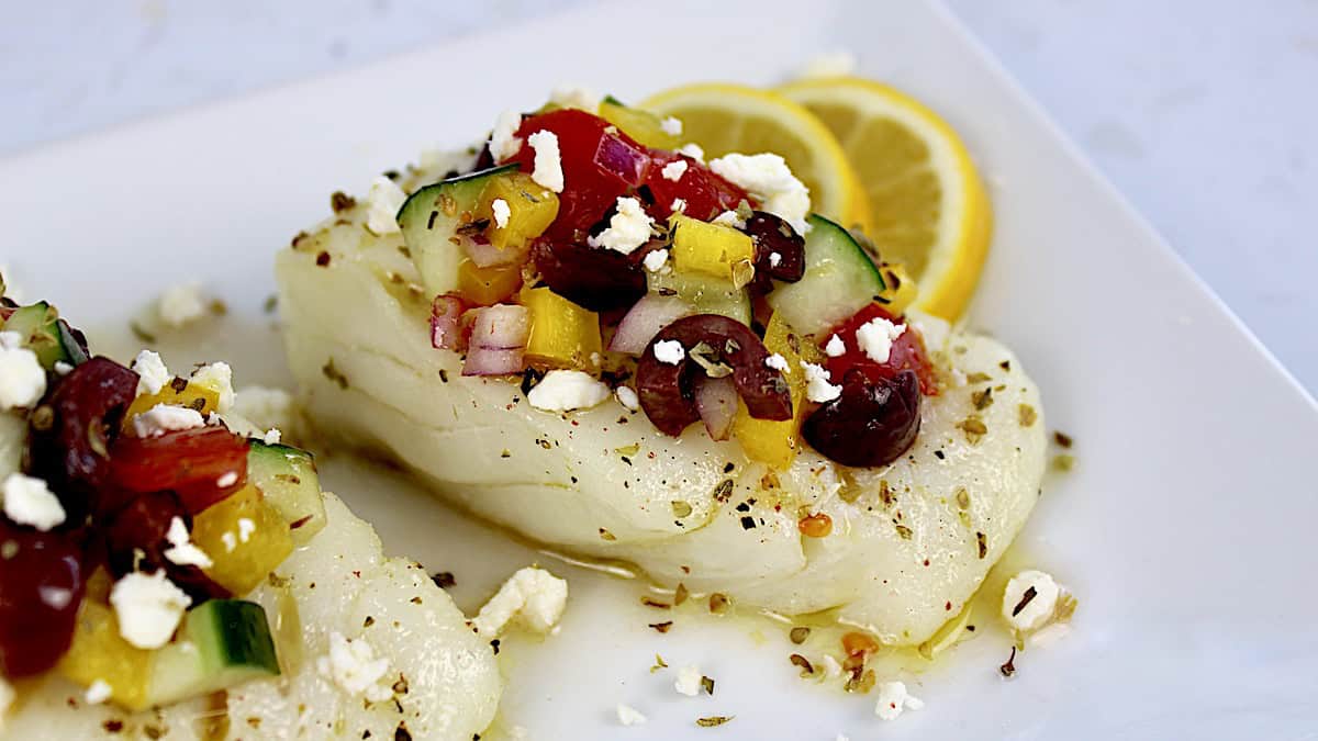 Baked Cod with Greek Salsa on white plate with 2 lemon slices