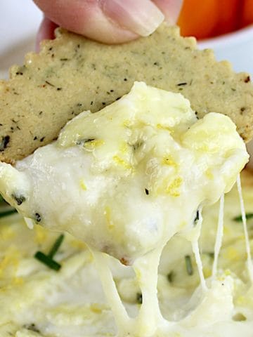 Baked Ricotta Dip with cracker being dipped in with cheese pulling up