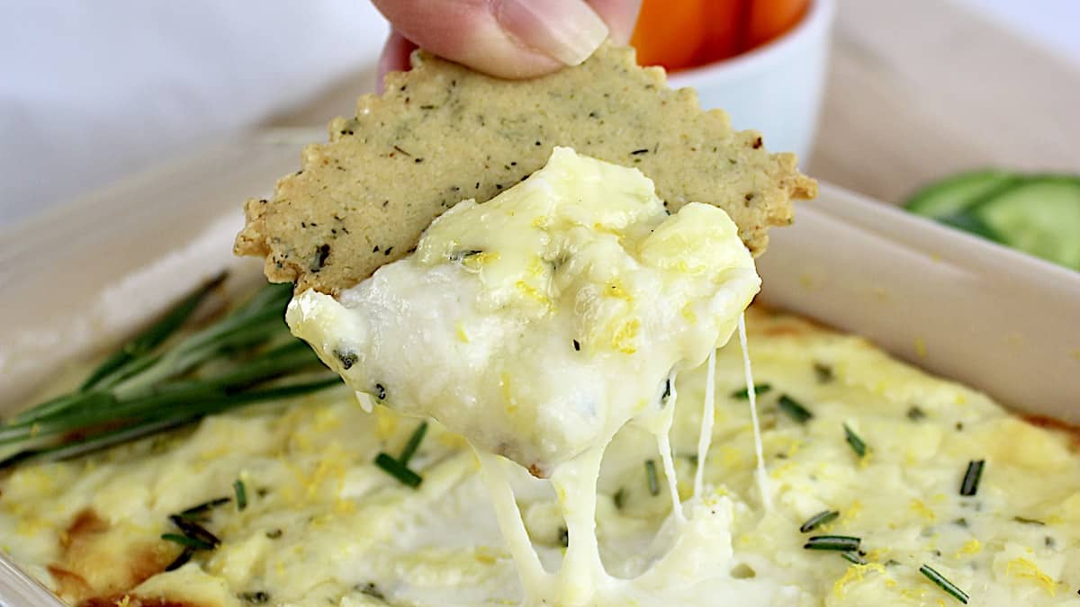 Baked Ricotta Dip with cracker being dipped in with cheese pulling up