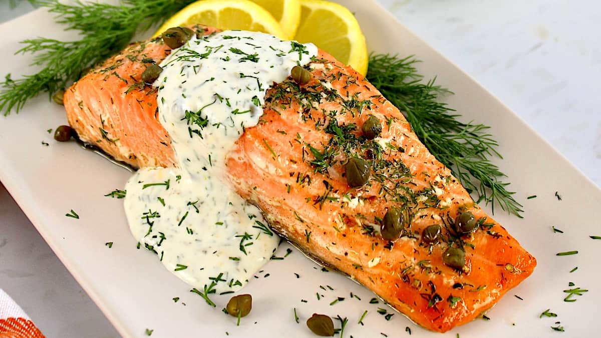 Baked Salmon with Creamy Dill Sauce over the top with capers, fresh dill and lemon slices on side