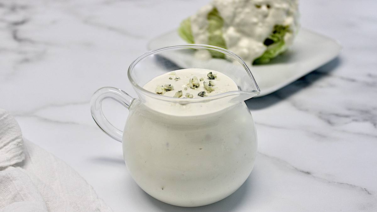 Blue Cheese Dressing in glass pitcher with salad in background