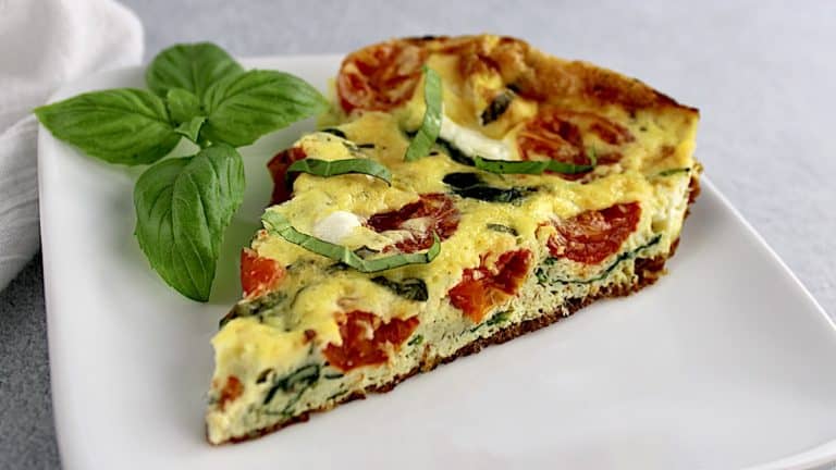 slice of Caprese Frittata on white plate with fresh basil garnish