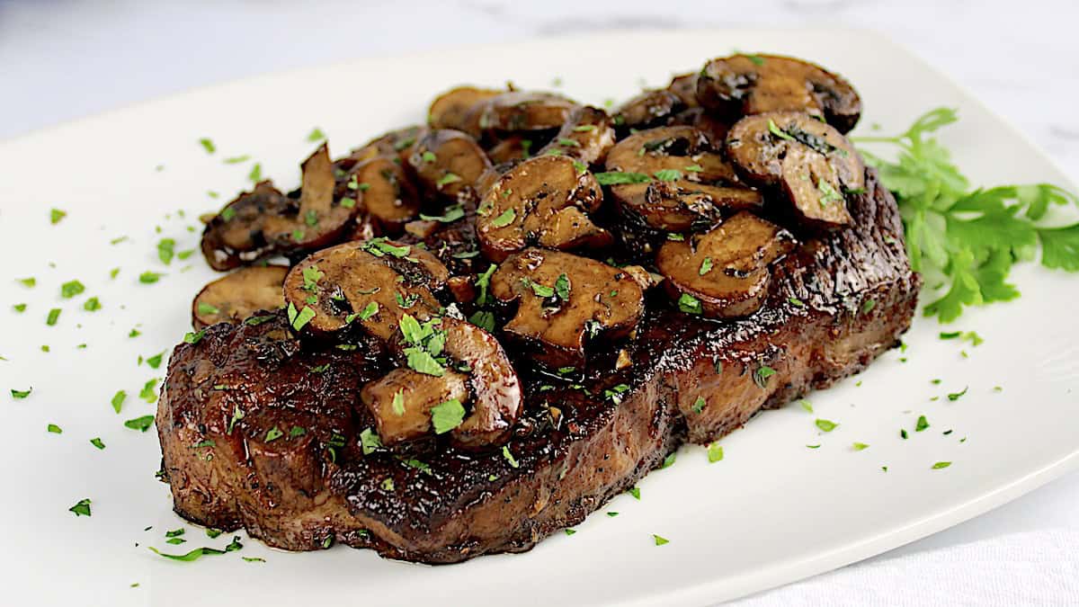 closeup of Cast Iron Steak and Mushrooms on white plate with parsley