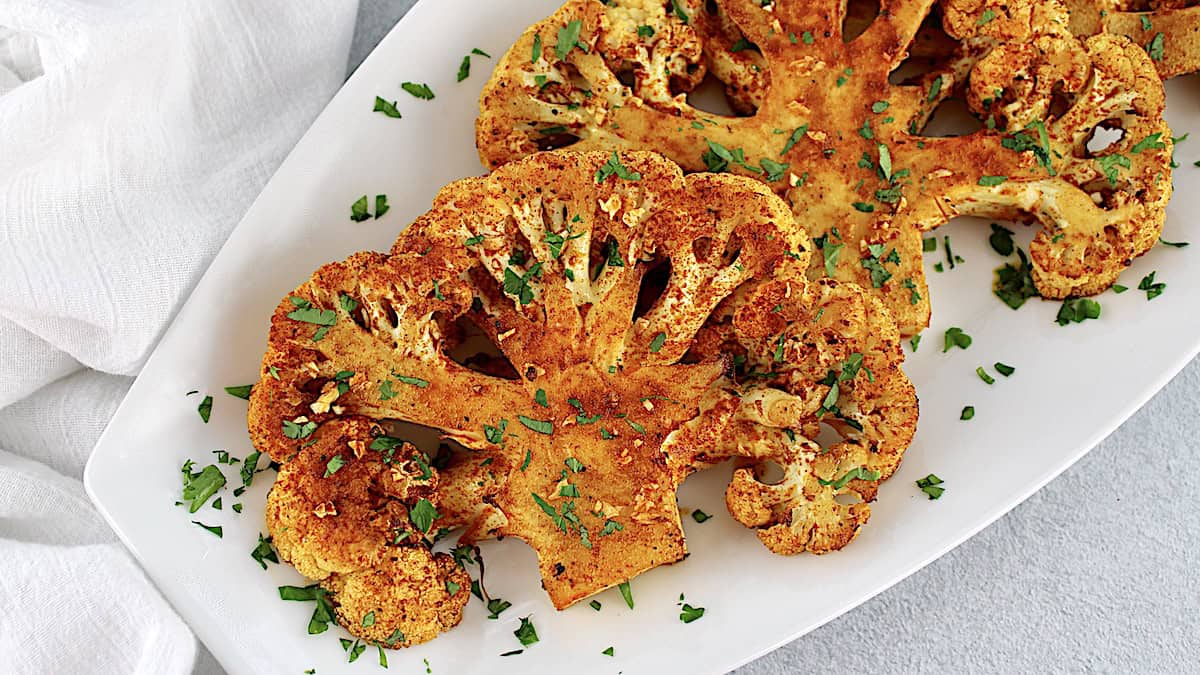 Cauliflower Steaks on white platter with chopped parsley