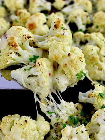 Cheesy Roasted Cauliflower being held up by silver spatula with cheese pull